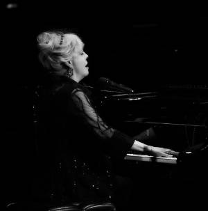 A picture of KT Sullivan playing piano in a spolight.